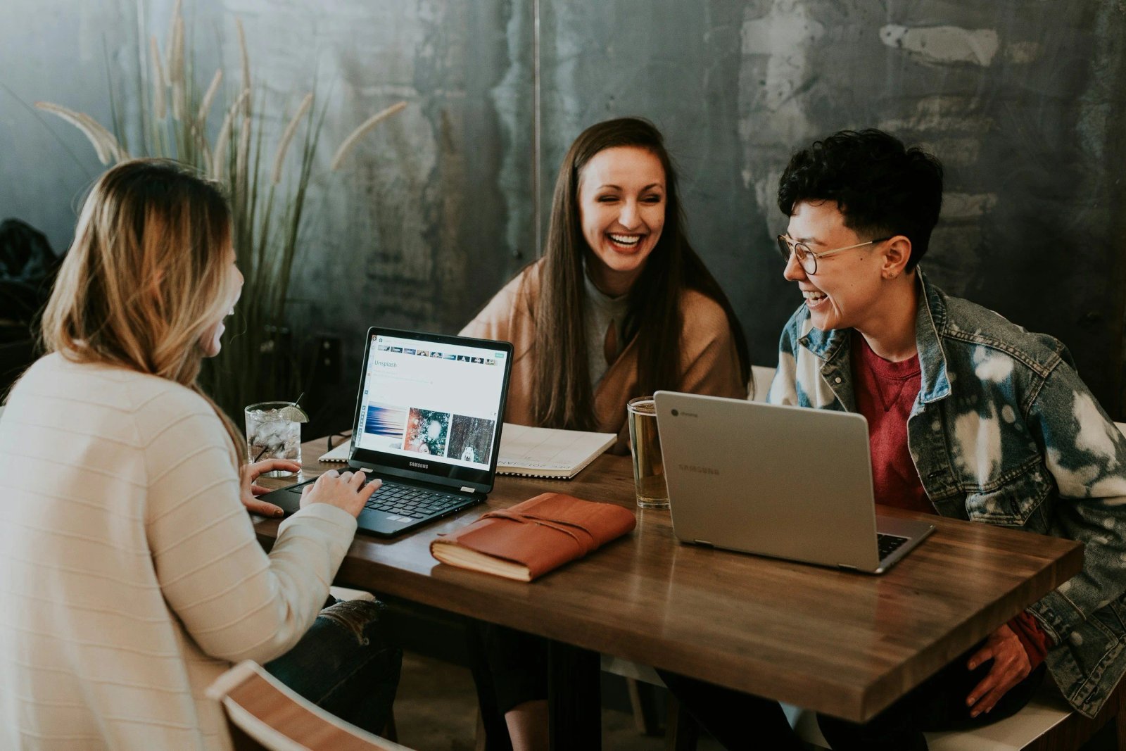Tres mujeres riendo y compartiendo una reunión de trabajo alrededor de una mesa con laptops
