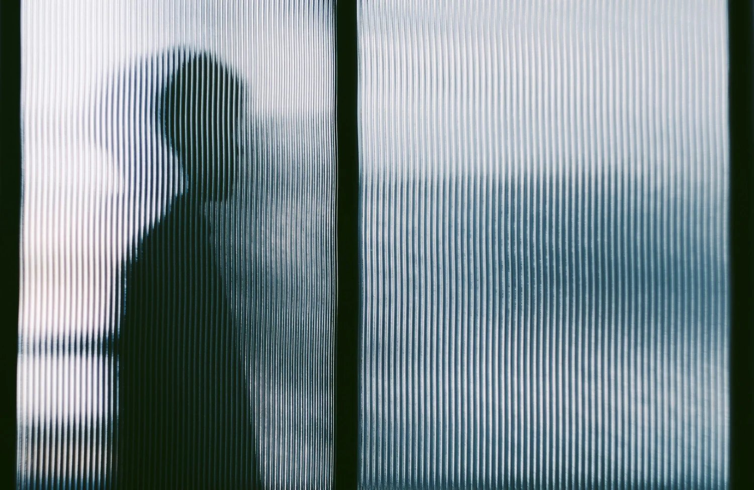 Silueta de una persona vista a través de una superficie traslúcida con líneas verticales